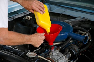 A person using a funnel to pour oil from a yellow container into a car engine.