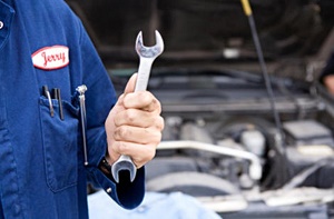 A car mechanic named Jerry holding a wrench in front of an open car hood.