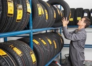 Person organizing labeled car tires on blue rack in auto shop